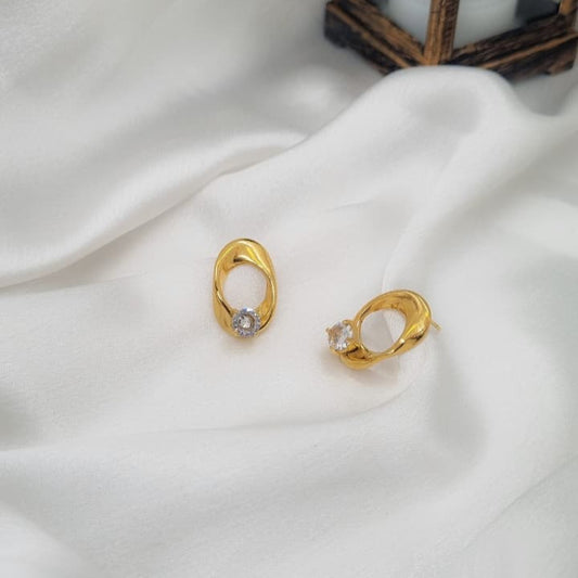Gold earrings with a central gemstone on a white fabric background
