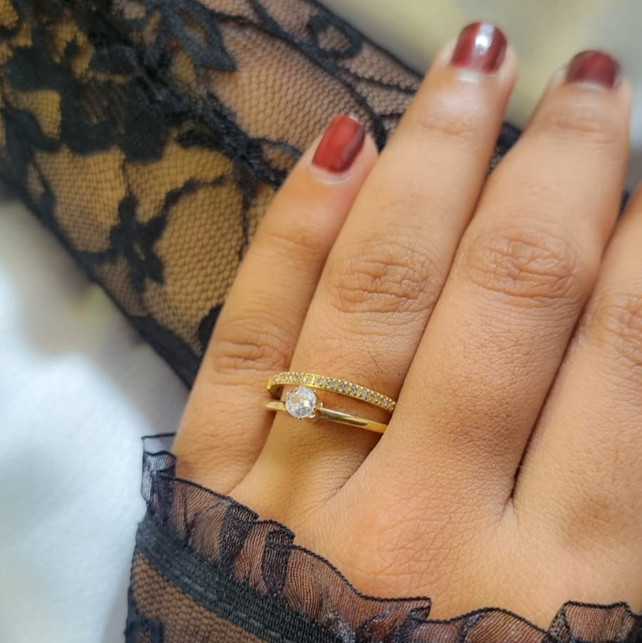 Hand wearing a gold ring with a diamond, against a black lace background
