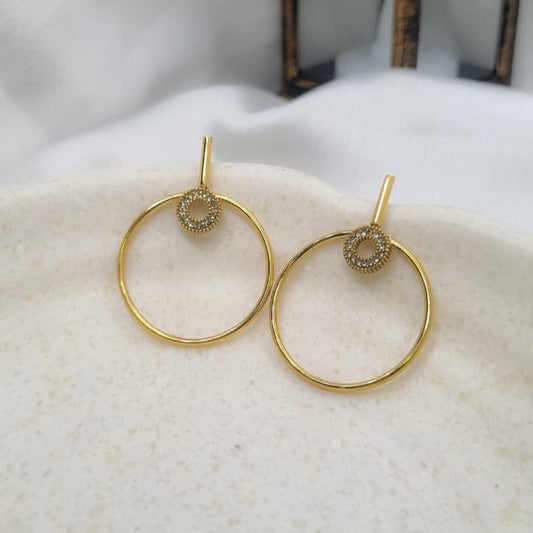 Gold hoop earrings with embedded stones on a textured white surface.