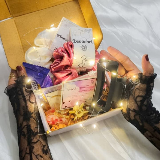 Hand holding a box of Devishri products with decorative lights on a white surface hamper gifting ideas wives sister gf 